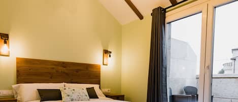 Une chambre d’hôtel avec une tête de lit en bois, un grand lit avec une literie blanche, deux lampes de chevet et une vue sur l’extérieur par une porte vitrée.