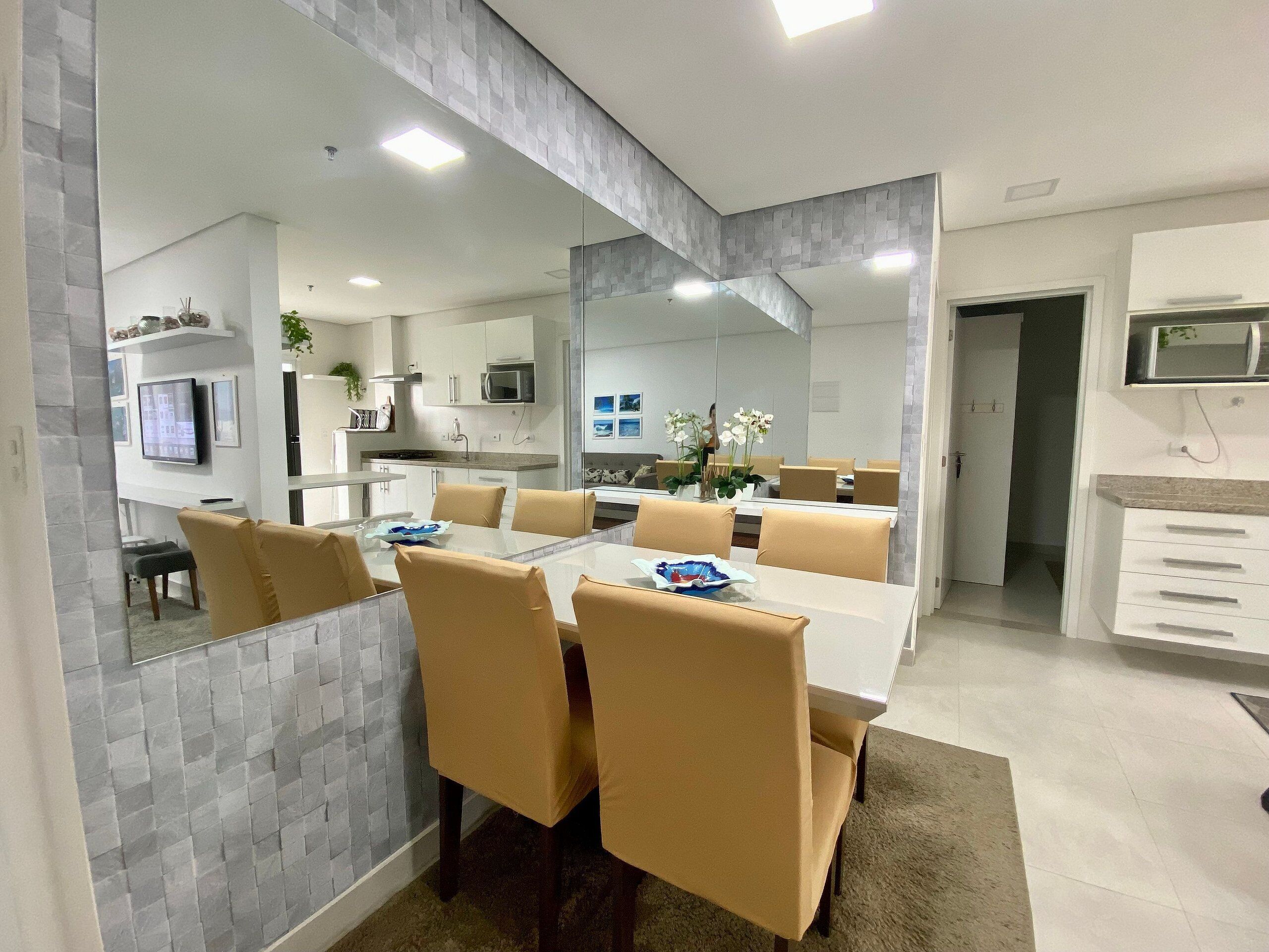 Un comedor moderno con una mesa de vidrio, sillas color beige y una cocina al fondo.