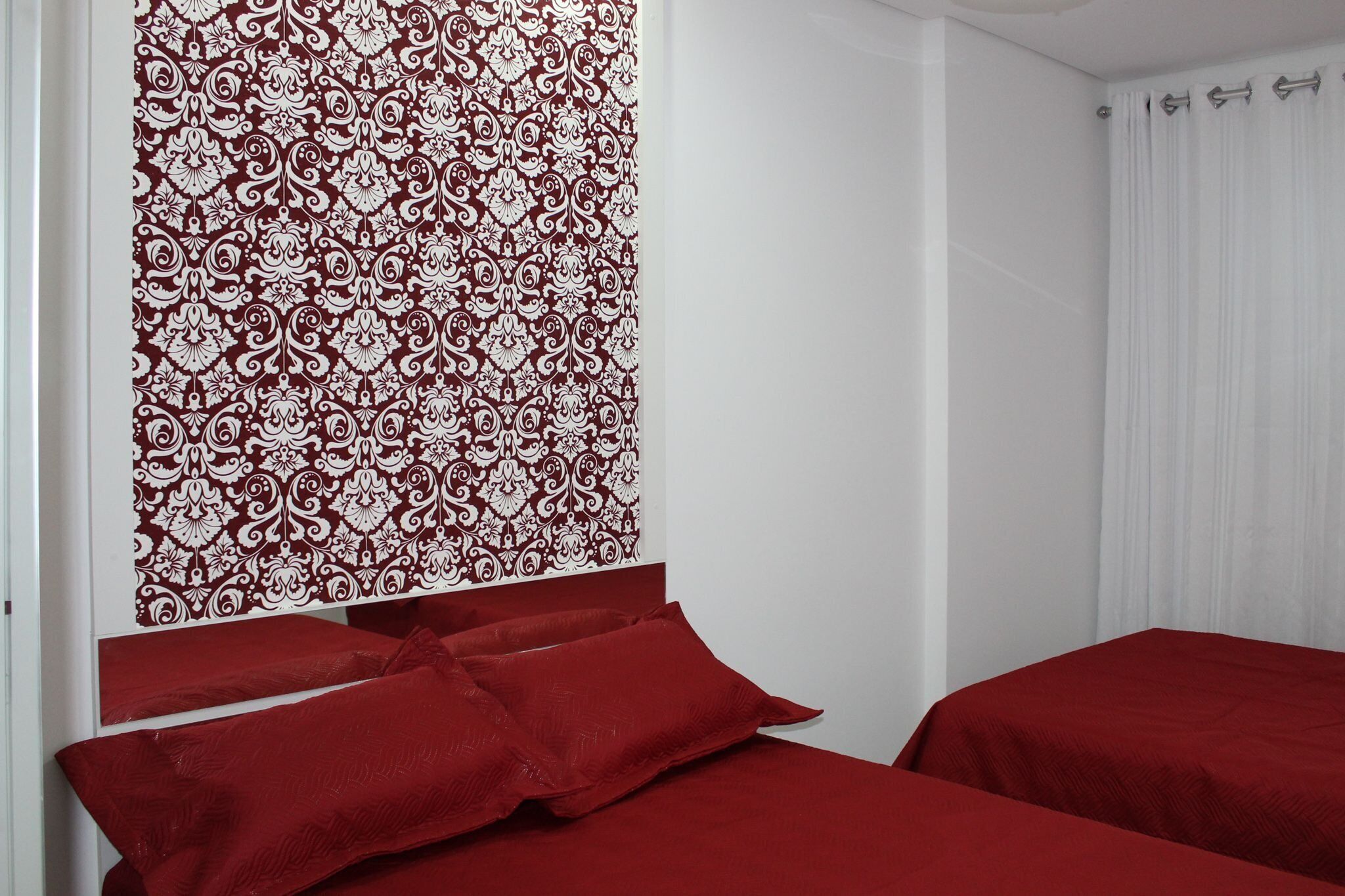 A room with two beds, a patterned wall, and a white curtain.