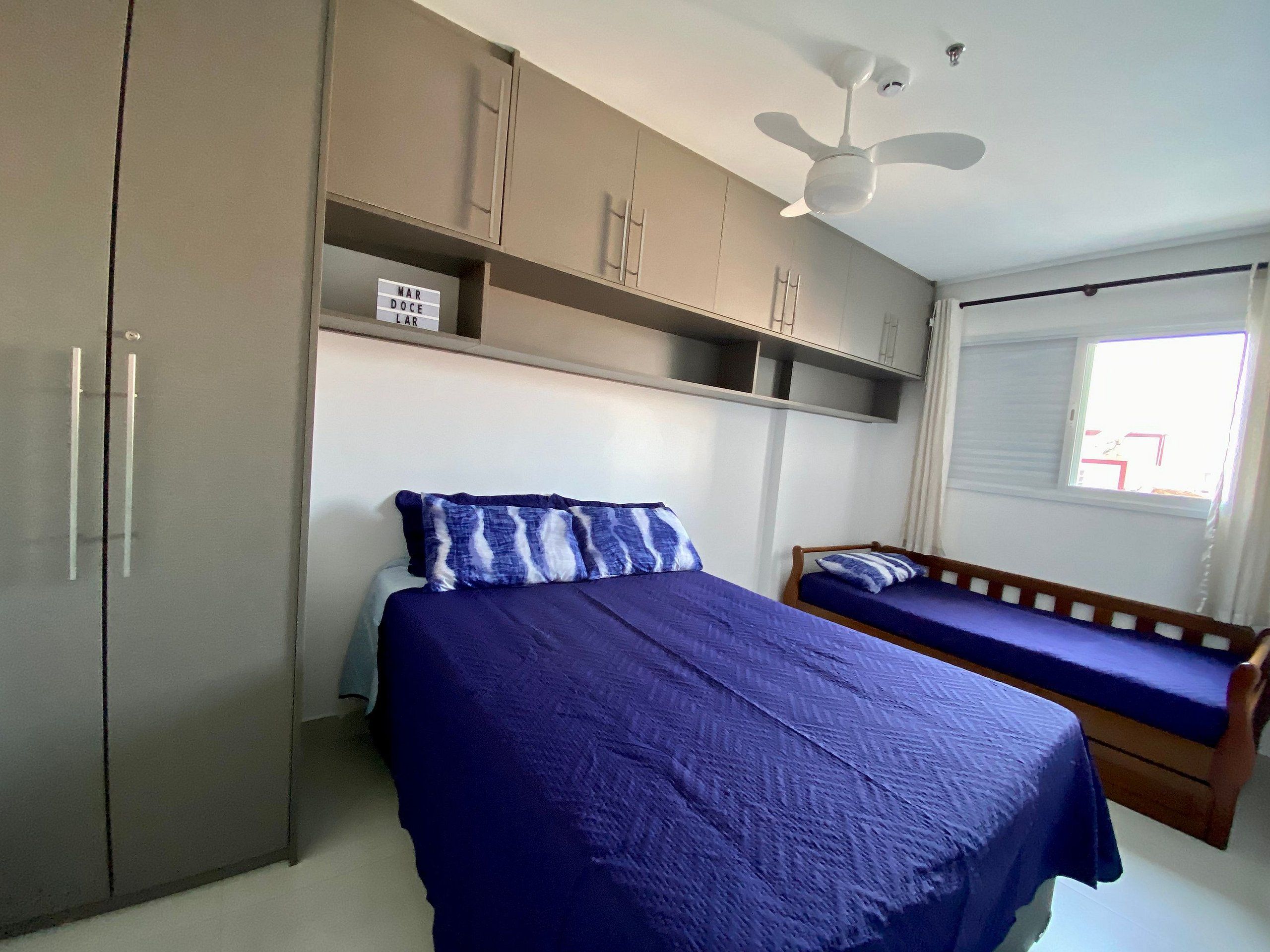 A bedroom with a bed, a wooden bench, a wardrobe, and a ceiling fan.