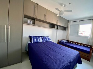 A bedroom with a bed, a wooden bench, a wardrobe, and a ceiling fan. - Flat Unitá Homestay (Praia Grande)