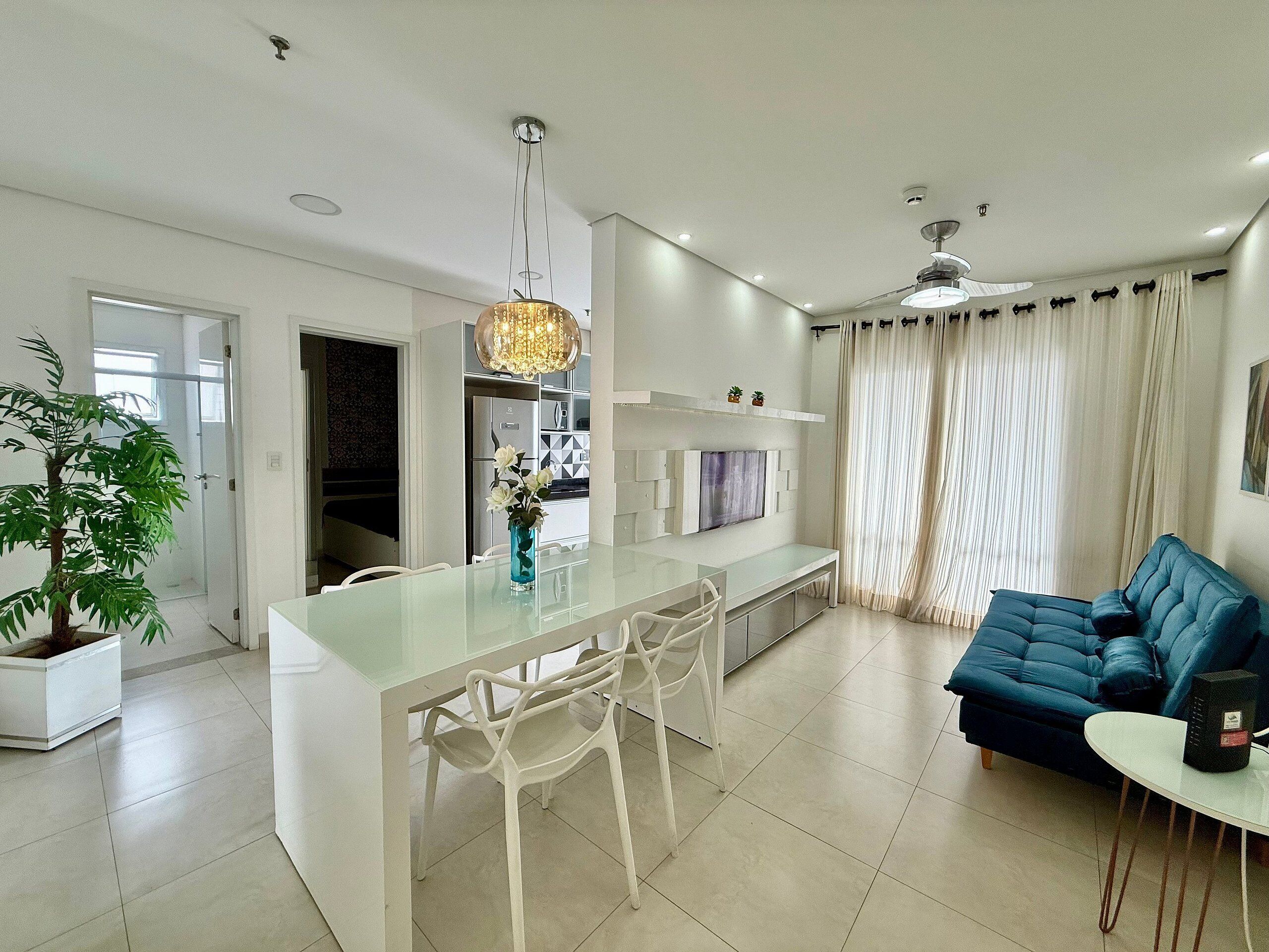 A modern living room with a sofa, a dining area with chairs, a TV, and a ceiling fan.