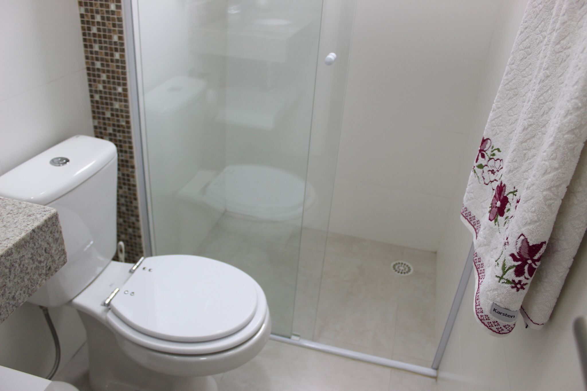 Un baño con inodoro, cabina de ducha y una toalla estampada con motivos florales.