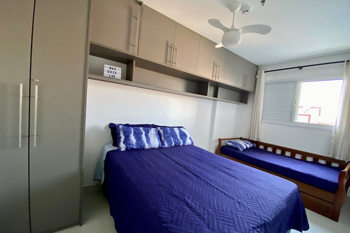 A bedroom with a bed, a wooden bench, a wardrobe, and a ceiling fan.