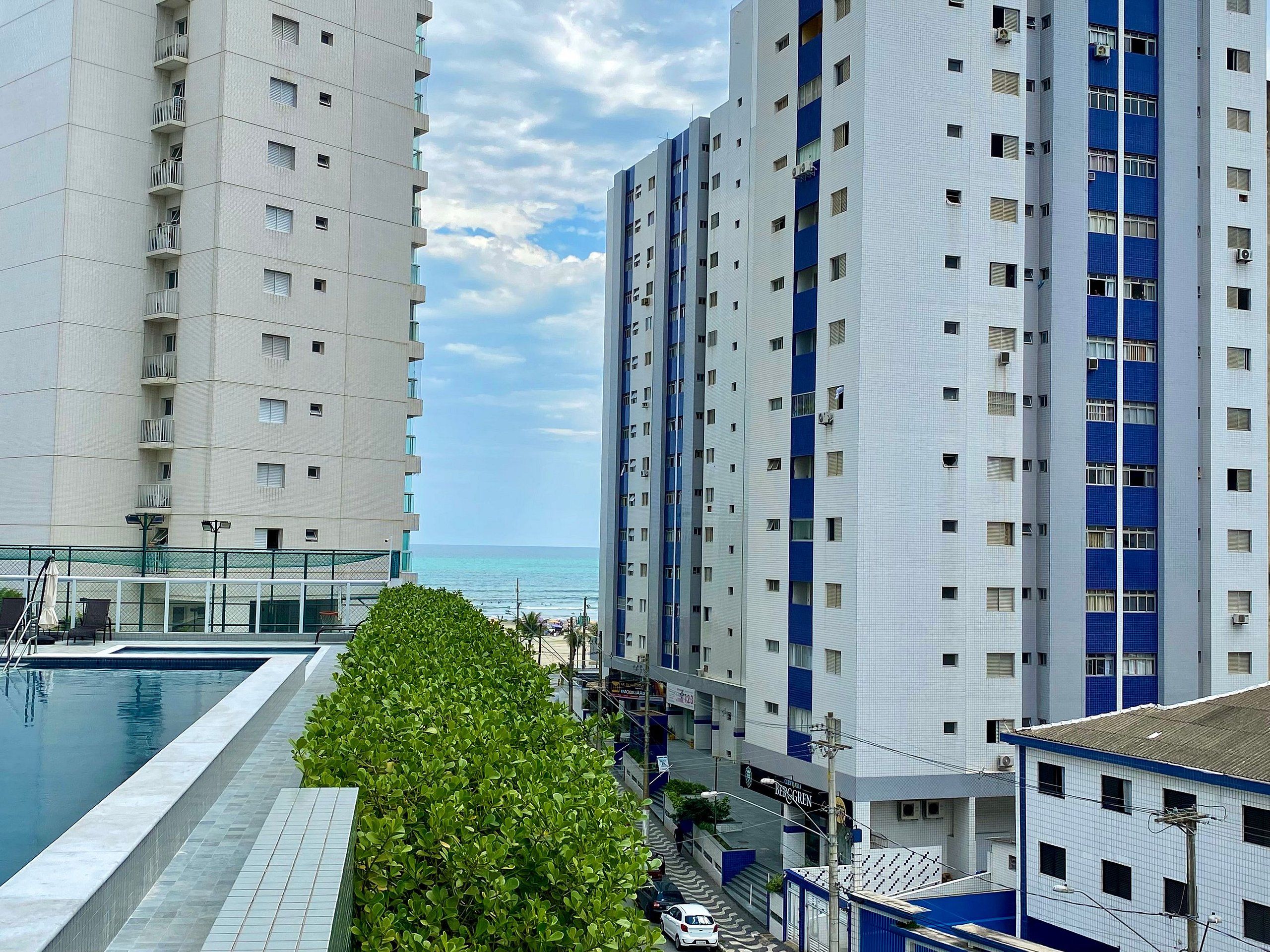 A high-rise building with multiple balconies, a swimming pool, and a view of the ocean.