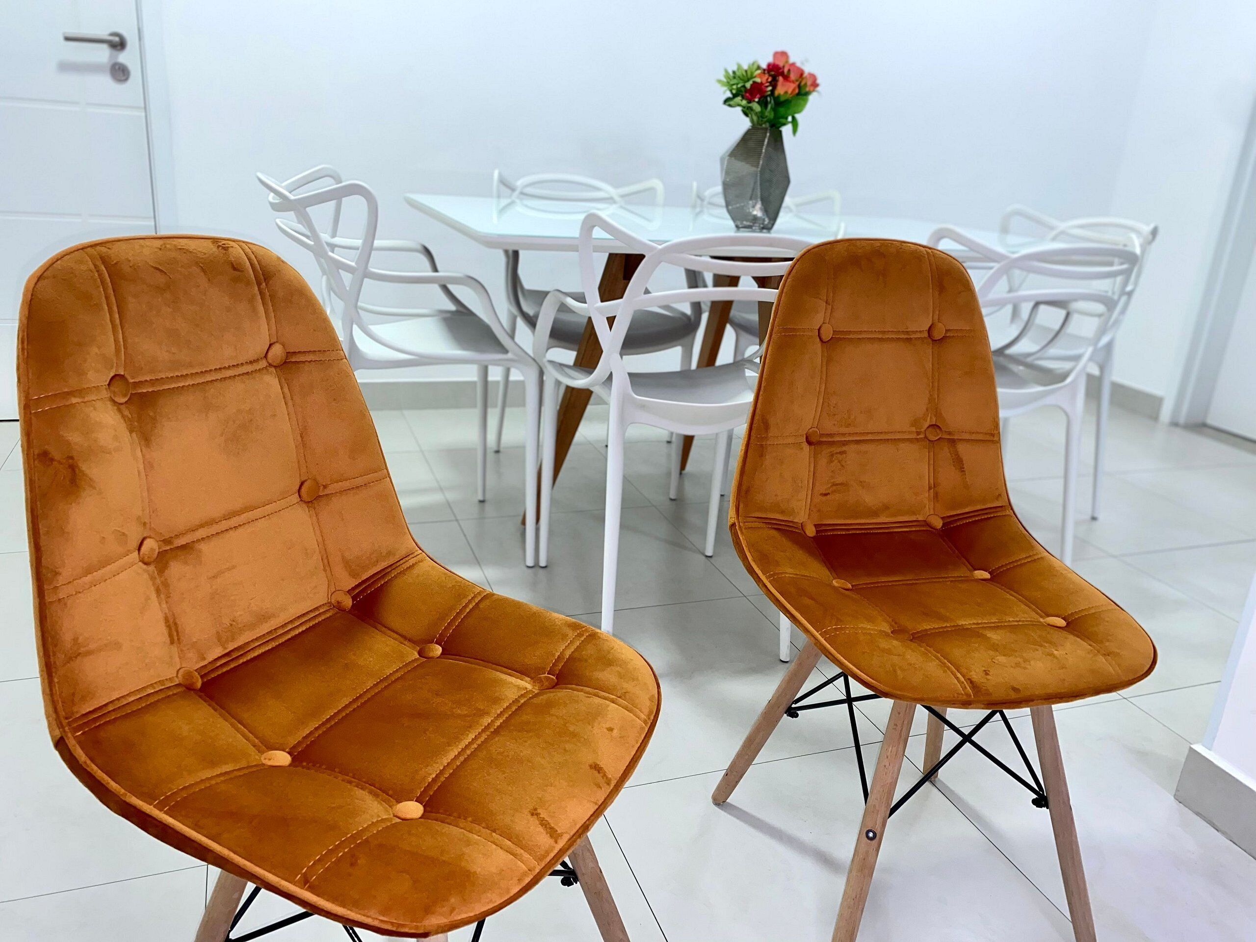 Dos sillas color mostaza con patas de madera y una mesa blanca con un florero de flores.