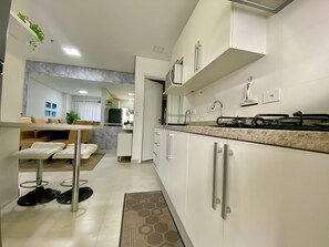 A modern kitchen with white cabinets, a stainless steel sink, and a countertop. - Flat Unitá Homestay (Praia Grande)