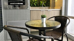 A kitchen with a built-in oven, a neon sign, a potted plant, and a round table with chairs. - Flat Unitá Homestay (Praia Grande)