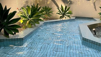A swimming pool with tiled flooring, surrounded by plants and a tiled wall.