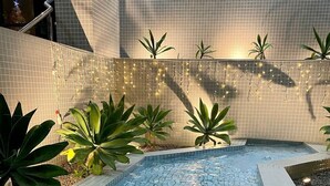 A swimming pool with tiled flooring, surrounded by plants and a tiled wall. - Flat Unitá Homestay (Praia Grande)