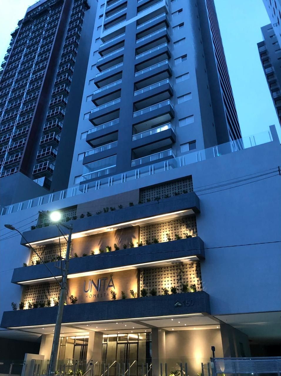 A high-rise building with a modern design, featuring balconies and a prominent entrance with a sign.