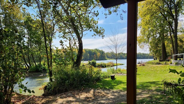 A lakeside view with a wooden deck, a covered seating area, and a path leading to the water. - Waterfront Cabin - Hot Tub - Free Bikes, Kyaks, Canoes, Paddle, & Fishing Boats! (Waterville)