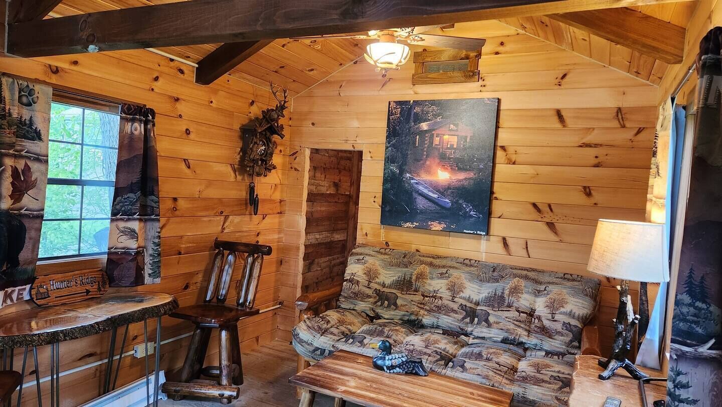 Een gezellig interieur van een blokhut met houten wanden, een hangklok, een open haard, een bank en een tafel met een lamp.