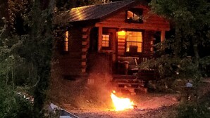 A wooden cabin with a fire in front, surrounded by trees. - Waterfront Cabin - Hot Tub - Free Bikes, Kyaks, Canoes, Paddle, & Fishing Boats! (Waterville)