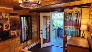 A wooden cabin interior with a large window, a door leading outside, and a wooden table with a lamp. - Waterfront Cabin - Hot Tub - Free Bikes, Kyaks, Canoes, Paddle, & Fishing Boats! (Waterville)