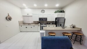 A modern kitchen with white cabinets, a stainless steel refrigerator, a stove, and a sink. There are three wooden stools at the counter. - Casamar 4 by Kivoya (Puerto Peñasco)