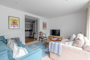Una sala moderna con sofá, televisor y comedor con mesa y sillas.