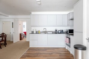Une cuisine moderne avec des meubles blancs, un îlot central et une poubelle en acier inoxydable.