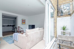 A modern living room with a sofa, a dining table, and a kitchen in the background. - Refurbished 2 Bed | Private Patio | Battersea (London)