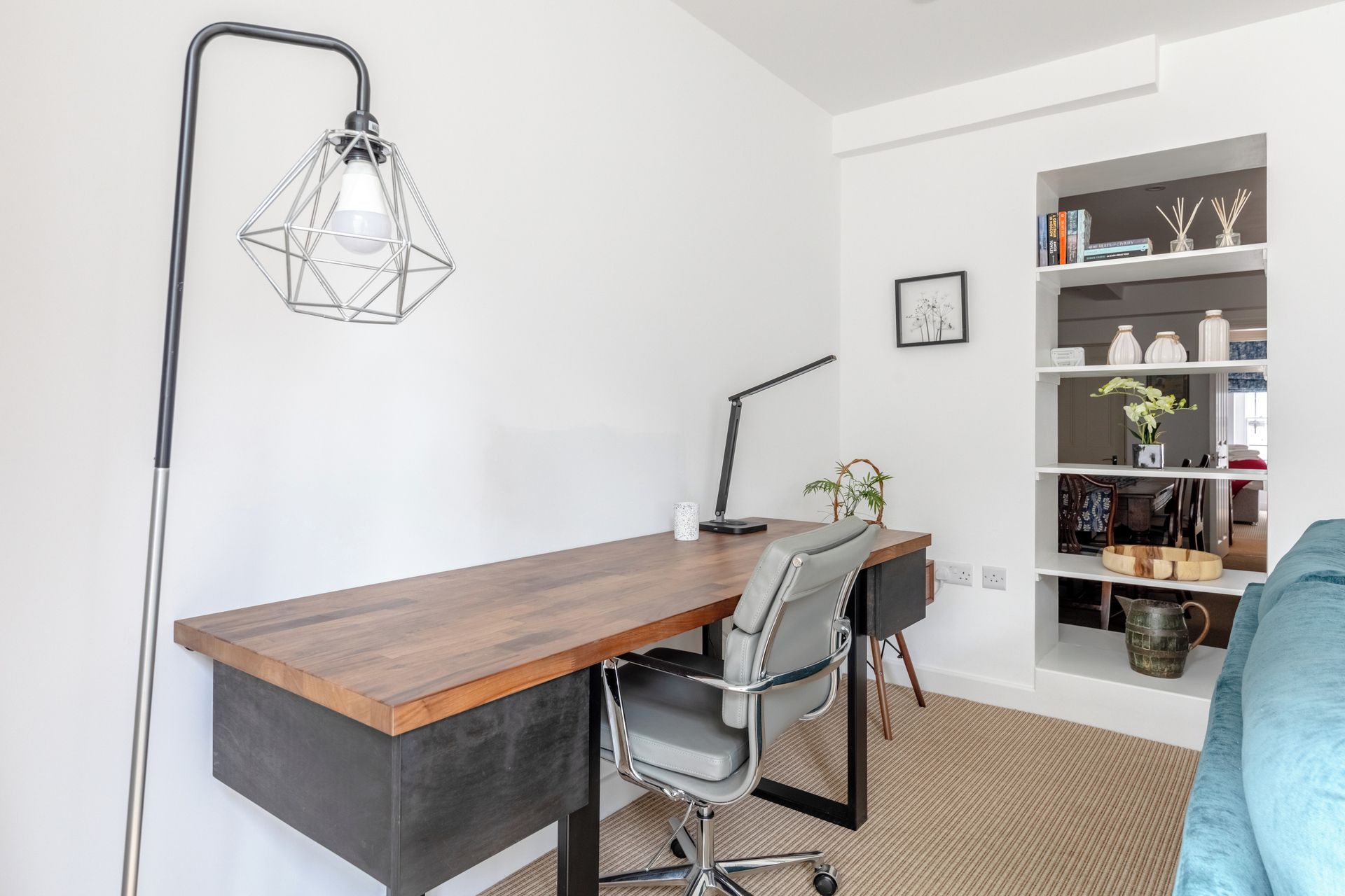 A modern office space with a wooden desk, a chair, a floor lamp, and a bookshelf.