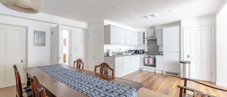 A spacious kitchen with white cabinets, a dining area with a wooden table and chairs, and a hanging light fixture.