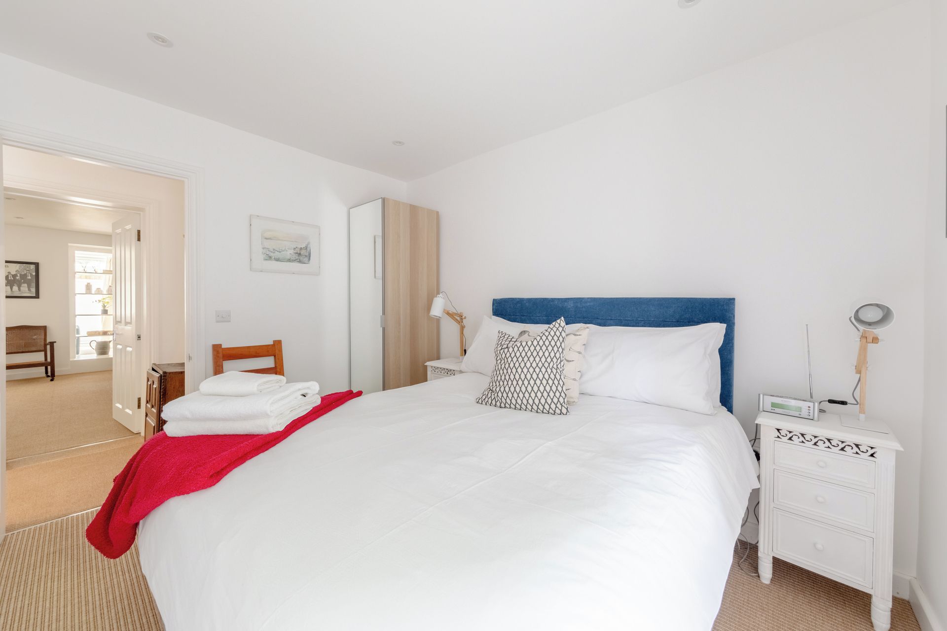 A hotel room with a large bed, a bedside table with a lamp, a nightstand with a digital device, and a door leading to a bathroom.