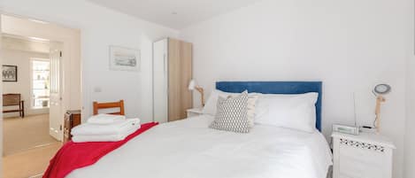 Une chambre d’hôtel avec un grand lit, une table de chevet avec une lampe, une petite table de nuit avec un appareil numérique, et une porte donnant sur une salle de bain.