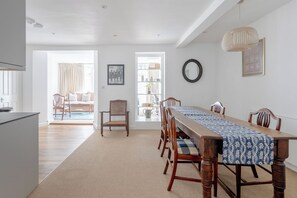 Un espace repas avec une longue table en bois, des chaises et un chemin de table à motifs.