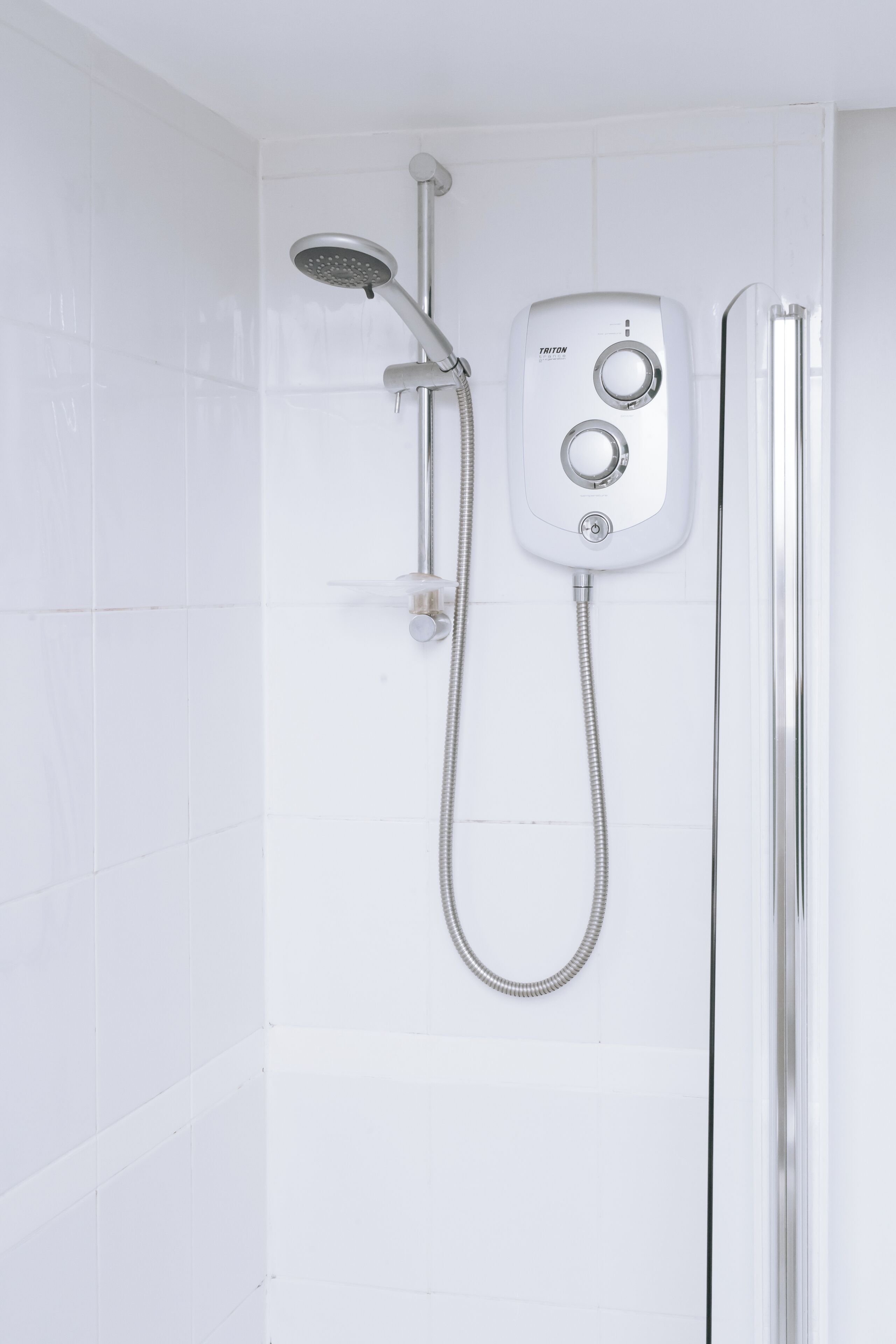 Um chuveiro moderno com um chuveiro manual e painel de controle, fixado em uma parede revestida de azulejos brancos.