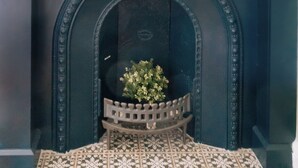 A dark-colored fireplace with a decorative mantel, a small bench, and a potted plant. - Stylish 1BD Flat - Abbeyhill (Edinburgh)