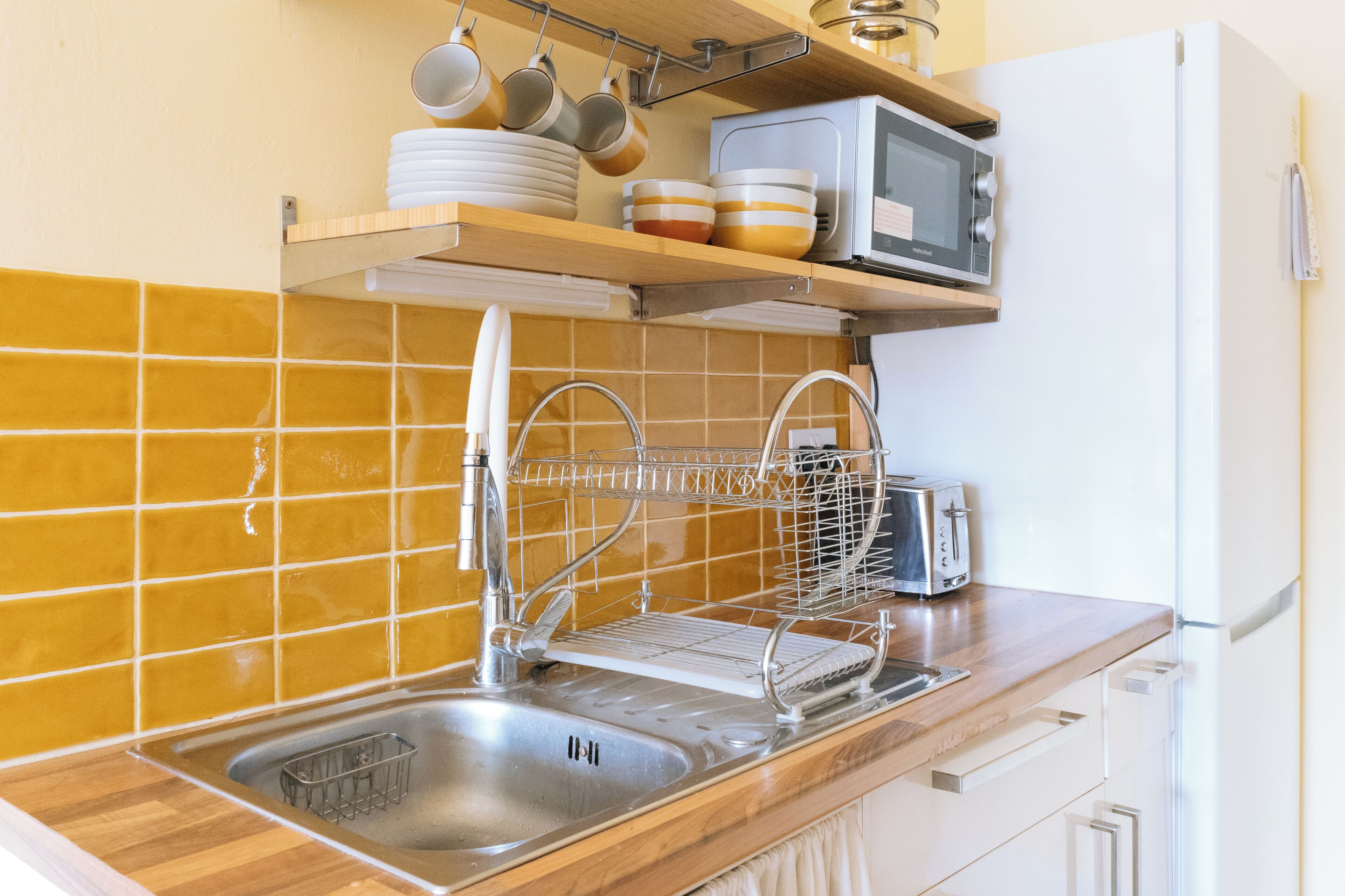 A kitchen with a stainless steel sink, a dish rack, a microwave, and a toaster.