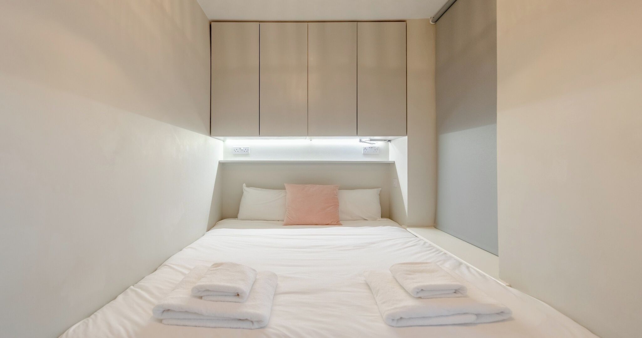 Una habitación de hotel pequeña y estrecha con una cama individual, un cabecero y un aplique de pared.