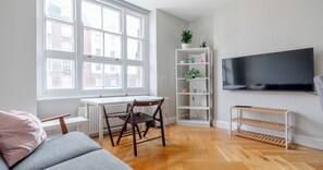 Ein modernes Wohnzimmer mit einer weißen Heizung, einem Esstisch mit Stühlen, einem grauen Sofa, einem an der Wand befestigten Fernseher und einem Holzboden.