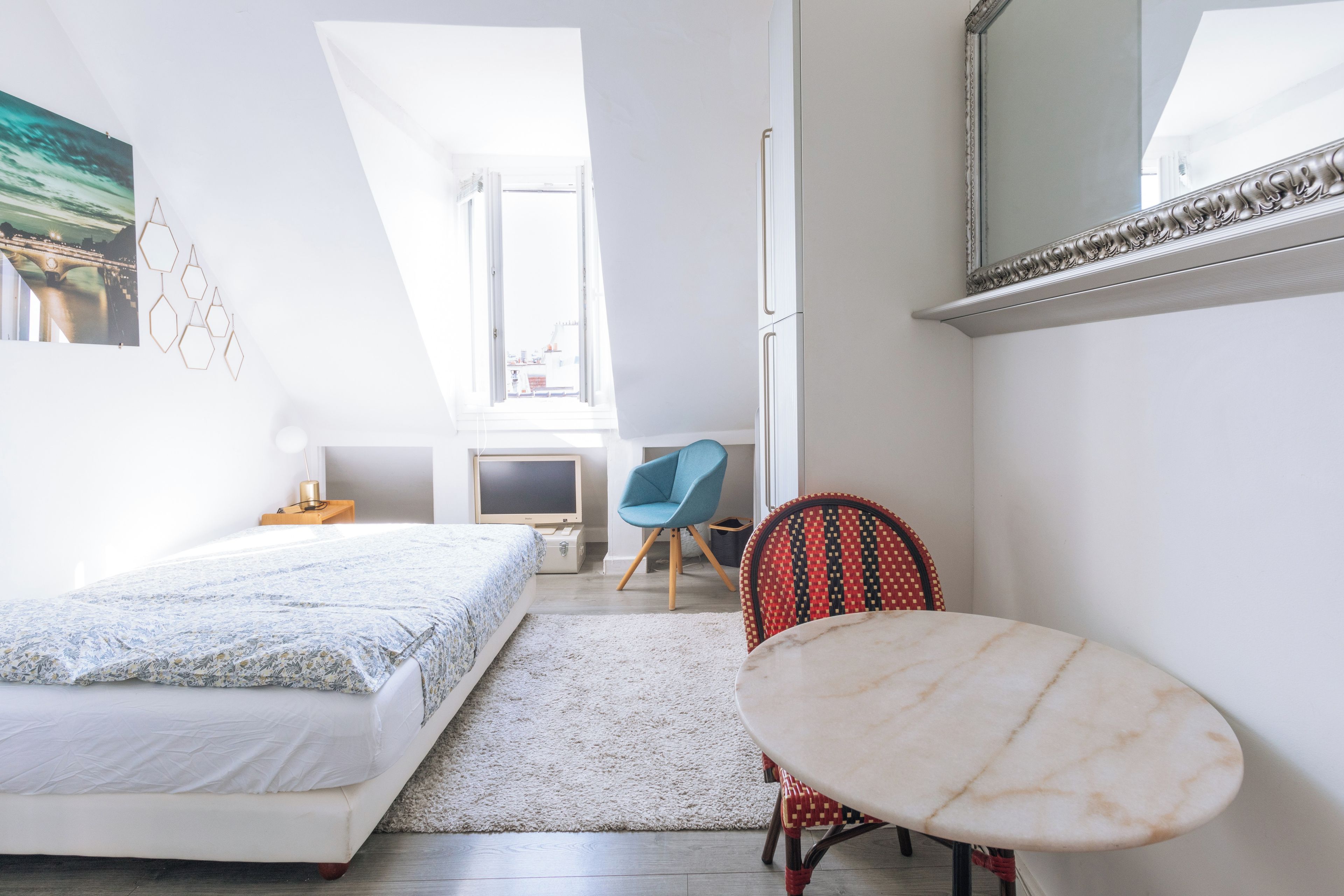 A bedroom with a bed, a desk, a chair, and a small table.