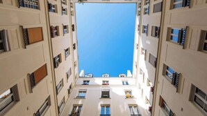 Un immeuble à plusieurs étages, doté de balcons, de grandes fenêtres et laissant apparaître un ciel bleu clair à travers l’ouverture centrale.