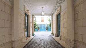 Un couloir au sol carrelé, avec un luminaire suspendu et une porte bleue au fond.