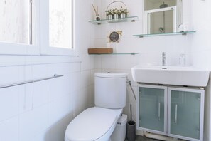 A modern bathroom with a toilet, a glass shelf with toiletries, and a glass shower enclosure. - Bright and Central Studio Apartment for 2, Paris (Paris)