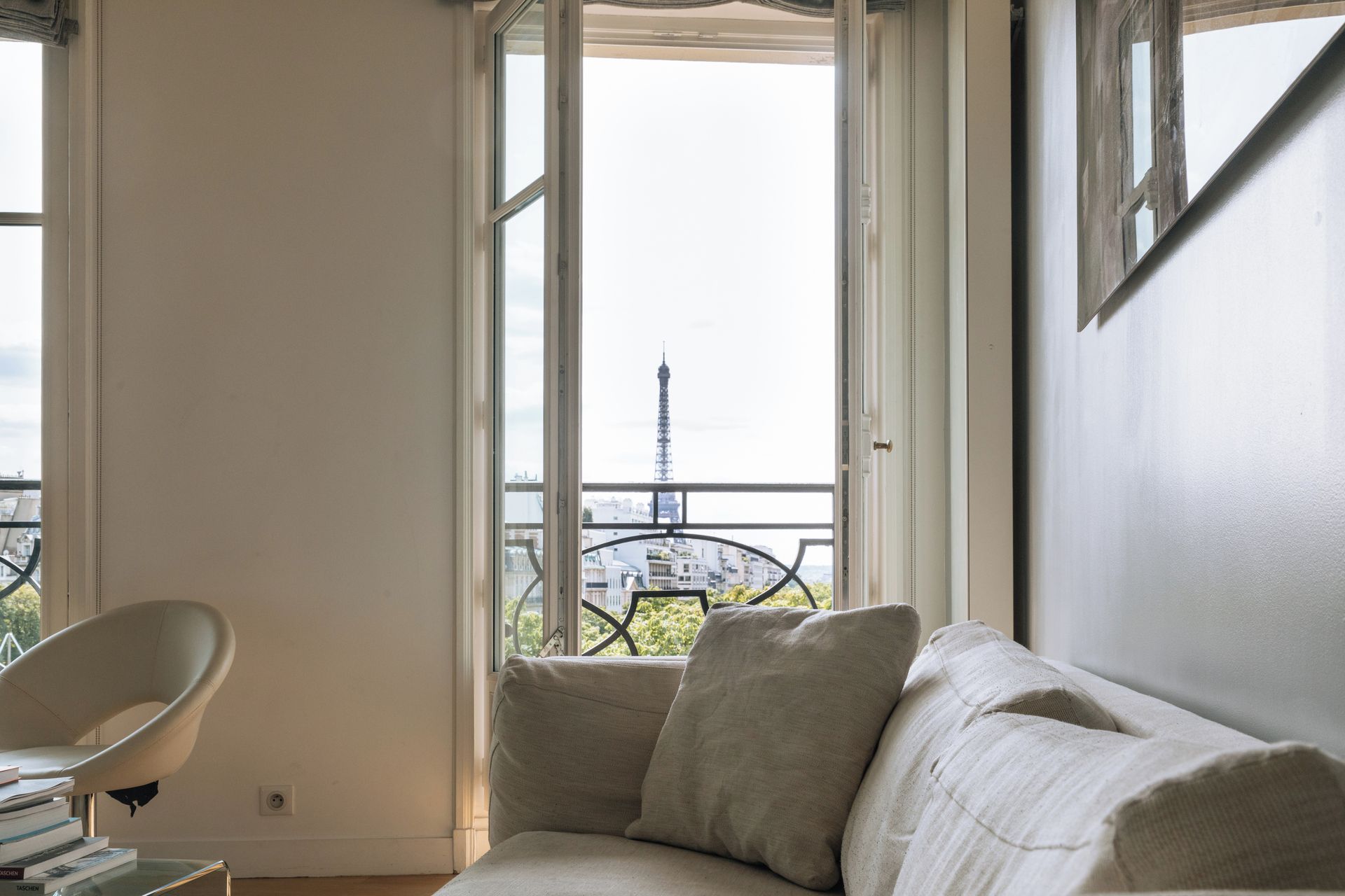 A room with a view of the Eiffel Tower, a white sofa, and a chair.