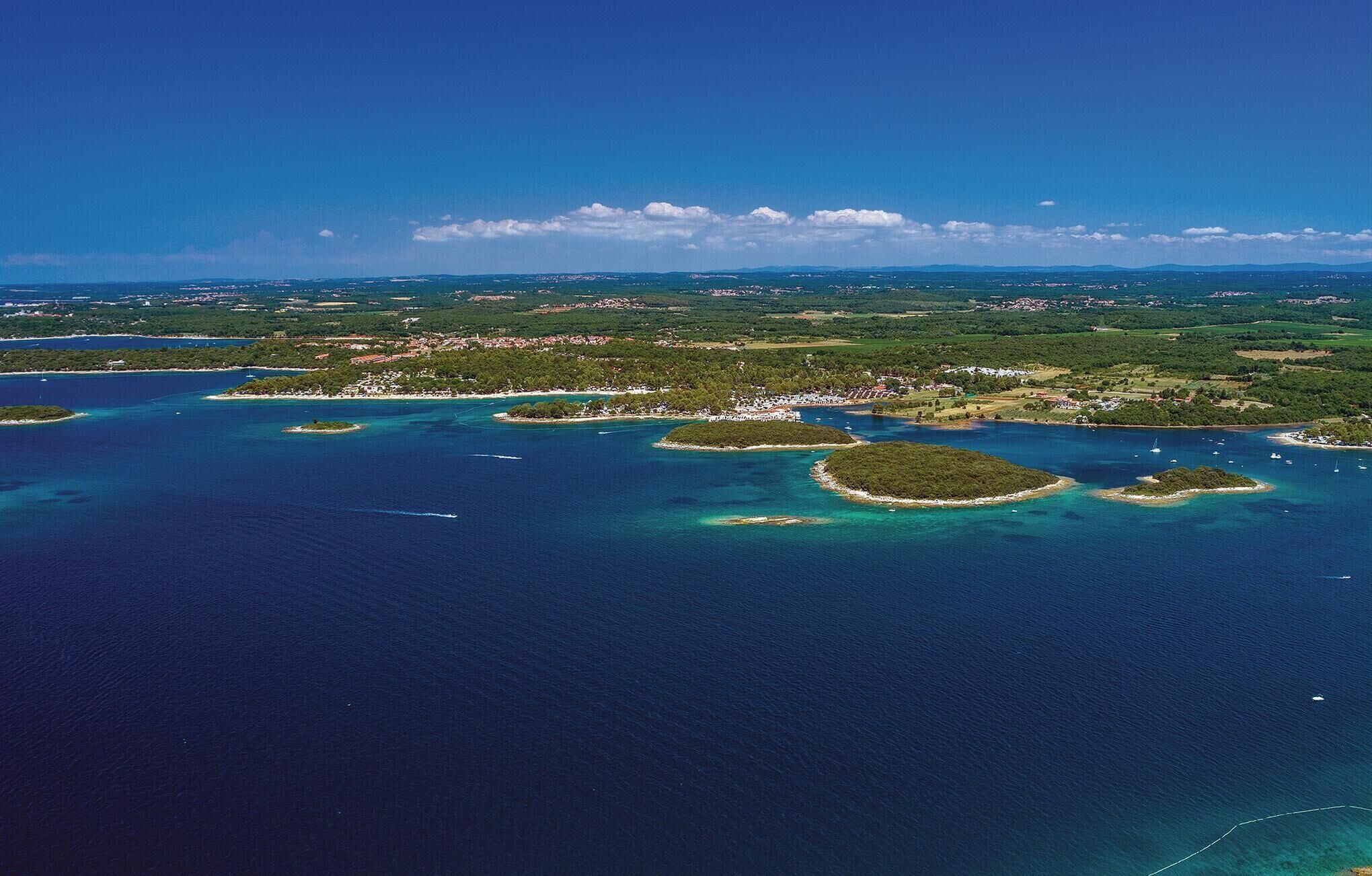 Luchtbeeld van een kustgebied met meerdere eilanden en helderblauw water.