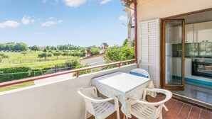 Een balkon met een tafel en stoelen, uitzicht op een groen landschap en een keukenhoek met een fornuis.