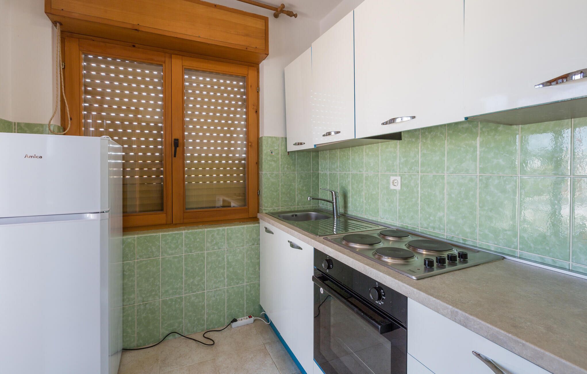 Una cocina compacta con refrigerador, estufa, lavamanos y paredes con azulejos verdes.