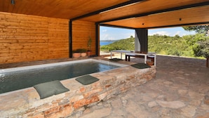 Ein Whirlpool mit Steinwänden, Holzboden und Blick auf das Meer.