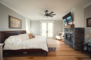 A bedroom with a bed, a ceiling fan, a stone fireplace, and a television mounted above it. - 🐎 Ann Riley Farmhouse | In Yuba Vineyards | Near GLEF | Trailer & Pet-Friendly | Game Room➠8062 (Williamsburg)