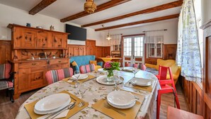 A dining room with a wooden table set for four, surrounded by colorful chairs, a wooden cabinet, and a large window with curtains. - Pet friendly home in Veliki Lovrecan with sauna (Veliki Lovrecan)