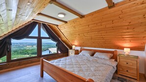 A bedroom with a sloped ceiling, wooden walls, a large window with a view, a bed, a nightstand, and a lamp. - Pet friendly home in Veliki Lovrecan with sauna (Veliki Lovrecan)