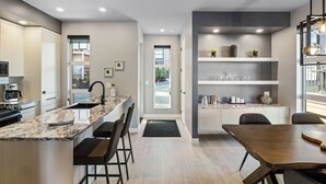 Een moderne keuken met een marmeren aanrecht, inbouwapparatuur en een eethoek met een houten tafel en stoelen.
