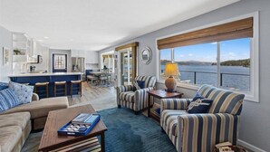 Een ruime woonkamer met een keuken, gestreept fauteuils, een bank en uitzicht op het water.
