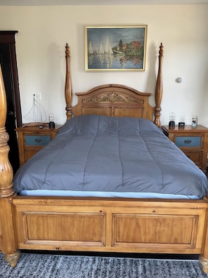 A wooden bed with a blue quilt, two nightstands with clocks, a painting of sailboats, and a door on the left. - Beachy Private Affordable Room LBI Long Beach Island Area Tuckerton West Creek  (Eagleswood)