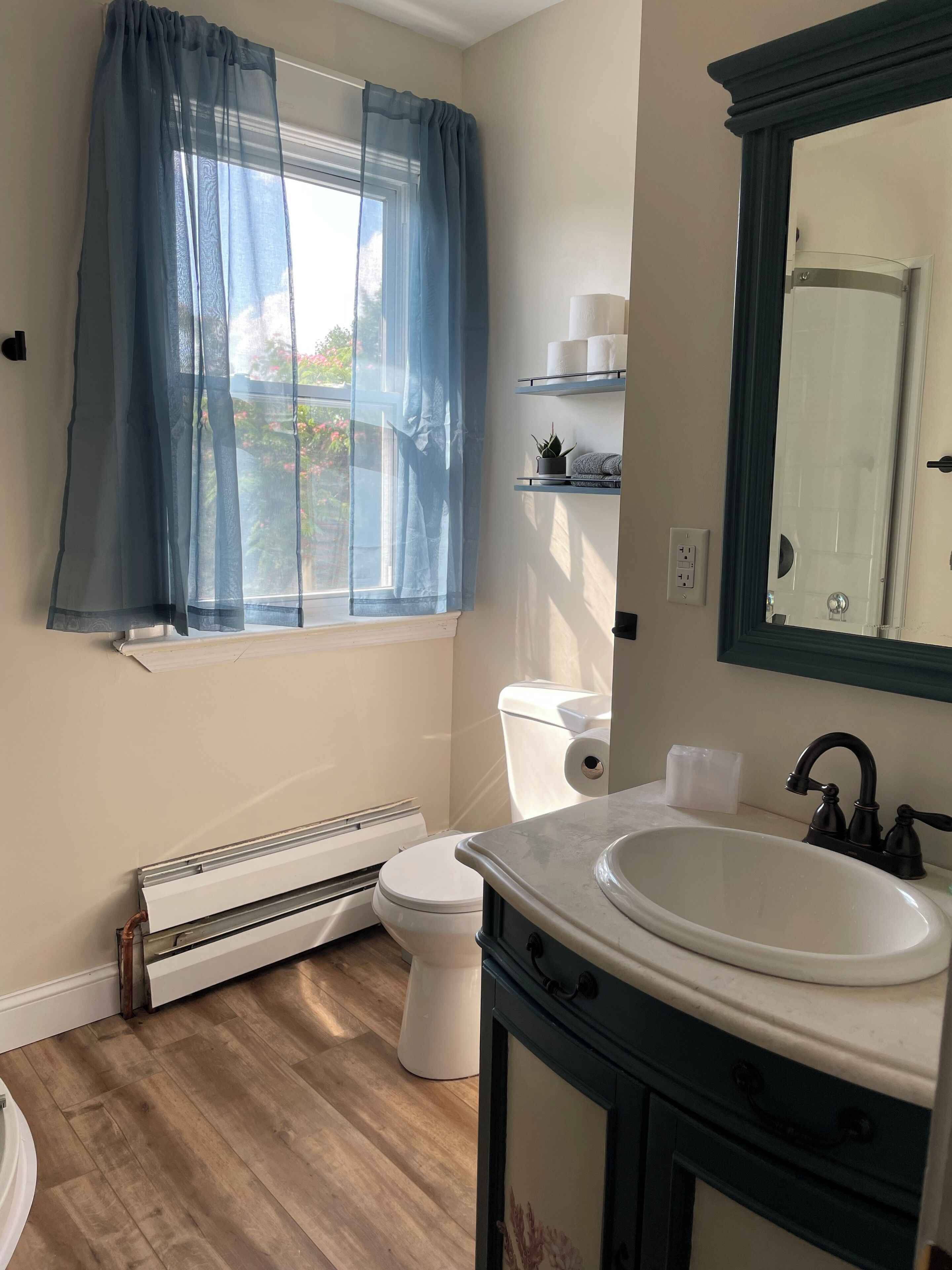 A bathroom with a window, toilet, radiator, sink, and mirror.