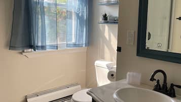 A bathroom with a window, toilet, radiator, sink, and mirror.